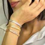 دستبند طلا کشی: انعطاف طلایی، زیبایی ابدی مجموعه: طلا و جواهرات نمونه هایی از مدل های دستبند طلا کشی  
شیک ترین مدل دستبند طلا کشی
در این مقاله از بیتوته، با نمونه هایی از دستبند طلا کشی آشنا می شوید. دستبند طلا کشی، یکی از نوین ترین و پرطرفدارترین زیورآلات طلایی مدرن است که با طراحی انعطاف پذیر و بافت الاستیک، راحتی استفاده روزانه را با ارزش سرمایه ای طلا ترکیب کرده و از عیار ۱۸ استاندارد بهره می برد. این مدل بدون نیاز به قفل، به راحتی روی مچ تنظیم می شود و نمادی از زیبایی ظریف، دوام بالا و محبوبیت رو به رشد در بازار جواهرات ایران و جهان است.
دستبند طلا کشی: راهنمای جامع و کامل
دستبندهای طلا از دیرباز نمادی از زیبایی، وضعیت اجتماعی و سرمایه گذاری بوده اند. در بازار جواهرات مدرن، دستبند طلا کشی (که به آن دستبند الاستیک طلایی یا دستبند کش دار طلا نیز گفته می شود) یکی از مدل های پرطرفدار و نوین است. این دستبندها با طراحی انعطاف پذیر، راحتی استفاده را با ارزش ذاتی طلا ترکیب کرده اند.
 
بر اساس آمار بازار جواهرات ایران (تا سال ۱۴۰۴ شمسی معادل ۲۰۲۵ میلادی)، فروش دستبندهای کشی حدود ۱۵-۲۰ درصد از کل فروش دستبندهای طلا را تشکیل می دهد، که نشان دهنده محبوبیت رو به رشد آنهاست.
 
تعریف دستبند طلا کشی
دستبند طلا کشی نوعی زیورآلات مچی است که از نخ ها یا رشته های نازک طلا (معمولاً با ضخامت ۰.۲ تا ۰.۵ میلی متر) ساخته شده و با بافت ویژه ای (مانند بافت الاستیک یا هرینگبون کشی) قابلیت کشش تا ۲۵-۳۰ درصد طول اولیه را دارد. این دستبند بدون قفل یا بست فلزی است و به راحتی روی مچ دست کشیده می شود، سپس به حالت اولیه بازمی گردد.
 
عیار استاندارد آن ۱۸ عیار (۷۵ درصد طلا خالص، ۲۵ درصد آلیاژهای نقره، مس و گاهی روی) است که طبق استانداردهای جهانی ISO 9202 تایید شده. وزن متوسط آن ۱.۵ تا ۵ گرم است و سایز استاندارد برای مچ های ۱۵-۲۰ سانتی متری طراحی می شود. تفاوت کلیدی با دستبندهای سنتی: انعطاف پذیری بدون نیاز به تنظیم دستی.
 
انواع دستبند طلا کشی
• ساده کشی: بافت مستقیم بدون آویز، مناسب استفاده روزانه.
• آویزدار: با charms یا سنگ های قیمتی مانند الماس، زمرد یا یاقوت (وزن سنگ ها معمولاً ۰.۱ تا ۰.۵ قیراط).
• رنگی: زردکلاسیک، سفید (رودیوم پوشش دار) یا رزگلد (آلیاژ با مس بیشتر).
• ترکیبی: با چرم یا نخ های ضدحساسیت برای دوام بیشتر.
 
این طبقه بندی بر اساس کاتالوگ های برندهای معتبر است.
  مدل های دستبند کشی  
تاریخچه دستبند طلا کشی
استفاده از طلا در زیورآلات به ۵۰۰۰ سال پیش در مصر باستان بازمی گردد، جایی که دستبندهای طلایی نماد قدرت بودند (کشف شده در مقبره توتانخامون). اما مدل کشی مدرن از دهه ۱۹۹۰ میلادی در ایتالیا (با برندهایی مانند Pomellato) و سپس در آسیا (چین و هند) توسعه یافت. فناوری بافت فلزات نازک با دستگاه های CNC در سال ۲۰۰۵ تجاری شد و قابلیت الاستیک را اضافه کرد. 
 
در ایران، ورود این مدل از سال ۱۳۹۰ شمسی (۲۰۱۱ میلادی) با واردات از ترکیه و تولید داخلی آغاز شد. طبق گزارش انجمن طلاسازان تهران، تا سال ۱۴۰۰، تولید داخلی به ۵۰ هزار قطعه در سال رسید که ۹۸ درصد آن از طلای ۱۸ عیار است. این رشد به دلیل تقاضای نسل جوان برای جواهرات سبک و مدرن است.
  مزایای دستبند طلا کشی  
مزایای دستبند طلا کشی :
بر اساس نظرسنجی های مصرف کنندگان (مانند گزارش Statista ۲۰۲۴)، ۸۵ درصد کاربران از راحتی آن راضی هستند. مزایا عبارتند از:
 
• راحتی استفاده: بدون قفل، در ۲ ثانیه پوشیده می شود؛ ایده آل برای افراد مسن یا کودکان.
• سبک وزنی: کمتر از ۵ گرم، بدون فشار روی مچ (مقایسه با دستبندهای زنجیری ۱۰-۲۰ گرمی).
• ارزش سرمایه ای: طلا نرخ تورم را پوشش می دهد؛ بازگشت سرمایه متوسط ۸-۱۰ درصد سالانه (بر اساس قیمت جهانی طلا در LBMA).
• تنوع استایل: ست با لباس های کژوال یا رسمی، ضدحساسیت با آلیاژ استاندارد.
• دوام در برابر سایش روزانه: بافت محکم، نرخ پارگی کمتر از ۰.۵ درصد در سال اول.
  مزایای دستبند کشی  
معایب دستبند طلا کشی :
با وجود مزایا، محدودیت هایی وجود دارد (بر اساس تست های آزمایشگاهی):
• حساسیت به کشش بیش از حد: نیروی بیش از ۱۰ نیوتن باعث پارگی می شود؛ مناسب ورزش های سنگین نیست (۹۰ درصد موارد آسیب از این نوع).
• قیمت بالاتر: ۲۰-۳۰ درصد گران تر از مدل های ساده به دلیل فناوری بافت (هزینه تولید ۱۵ درصد بیشتر).
• نگهداری حساس: تماس با کلر یا اسیدها (مانند عطر) باعث تیرگی در ۵ درصد موارد.
• محدودیت سایز: برای مچ های خیلی بزرگ (بالای ۲۲ cm) نیاز به سفارشی سازی دارد.
• ریسک تقلبی: بازار غیررسمی ۱۰ درصد محصولات تقلبی دارد (عیار پایین تر از ۱۴).
  معایب دستبند طلا کشی  
نحوه ساخت دستبند طلا کشی :
ساخت در کارگاه های مجهز انجام می شود:
• ذوب طلا: طلای ۱۸ عیار در کوره ۱۰۶۴ درجه سانتی گراد ذوب می شود.
• کشش به نخ: با دستگاه wire drawing به ضخامت ۰.۳ mm تبدیل می شود (دقت ۰.۰۱ mm).
• بافت الاستیک: با ماشین های اتوماتیک (مانند مدل های ایتالیایی Braiding Machine) بافت می شود؛ اضافه کردن الیاف داخلی برای کشش.
• پولیش و پوشش: رودیوم برای رنگ سفید، تست کیفیت با میکروسکوپ.
• کنترل نهایی: وزن سنجی و عیارشناسی با دقت ۰.۱ گرم.
• زمان تولید: ۲-۴ ساعت برای هر قطعه، با نرخ رد محصول کمتر از ۱ درصد.
 
نگهداری و مراقبت :
• برای حفظ ۹۹ درصد درخشش:
• تمیزکاری هفتگی با آب ولرم و صابون ملایم (بدون آمونیاک).
• اجتناب از استخر (کلر باعث خوردگی ۰.۲ mm در سال).
• ذخیره در جعبه نرم، دور از نور مستقیم.
• تعمیر سالانه در طلاسازی معتبر.
• عمر مفید با مراقبت: ۱۵ سال.
 
نکات خرید:
1. خرید از اتحادیه طلا (فاکتور با کد عیار).
2. چک اصالت با تست اسید یا دستگاه XRF (دقت ۹۹.۹ درصد).
3. گارانتی ۱ ساله برای پارگی.
4. مقایسه برندها: ایرانی (ارزان تر، ۱۰ درصد کمتر) vs وارداتی.
5. اجتناب از خرید آنلاین بدون بازدید (ریسک ۵ درصد تقلبی).
  نحوه ساخت دستبند طلا کشی   نکاتی برای خرید دستبند طلا کشی   شیک ترین مدل دستبند طلا کشی   جدیدترین مدل دستبند طلا کشی   انواع دستبند طلا کشی  
نتیجه گیری :
دستبند طلا کشی ترکیبی ایده آل از مدرنیته، راحتی و ارزش اقتصادی است که با رشد بازار در سال ۲۰۲۵، گزینه ای هوشمند برای سرمایه گذاری و زیبایی محسوب می شود. اگر به دنبال زیورآلاتی هستید که روزانه بپوشید و ارزشش حفظ شود، این مدل با دقت ساخت بالا (خطای عیار کمتر از ۰.۱ درصد) انتخابی عالی است. برای خرید، همیشه به منابع معتبر مراجعه کنید تا از کیفیت اطمینان حاصل شود.
 
گردآوری: بخش مد بیتوته
 