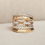 مدل انگشتر پورتوفینو: نمادی از لوکس گرایی و طراحی ایتالیایی مجموعه: طلا و جواهرات مدل انگشتر پورتوفینو: نمادی از لوکس گرایی و طراحی ایتالیایی  
نمونه هایی از شیک ترین مدل انگشترهای پورتوفینو
در این مقاله از بیتوته، با نمونه هایی از مدل انگشتر پورتوفینو آشنا می شوید. انگشتر پورتوفینو، الهام گرفته از زیبایی های ساحلی شهر پورتوفینو در ایتالیا، نمادی از لوکس گرایی و طراحی مینیمال چندحلقه ای است. این مدل با ترکیب سادگی و درخشش، به یکی از ترندهای جهانی جواهرات تبدیل شده و مورد توجه سلبریتی ها قرار گرفته است.
مدل های انگشتر پورتوفینو: نمادی از لوکس گرایی و طراحی ایتالیایی
انگشتر پورتوفینو، به عنوان یکی از برجسته ترین مدل های زیورآلات لوکس در دنیای مد و جواهرسازی، الهام گرفته از زیبایی های طبیعی و فرهنگی شهر ساحلی پورتوفینو در ایتالیا است. این شهر، واقع در منطقه لیگوریا، با مناظر خیره کننده، آب های فیروزه ای و فضای رمانتیک خود، به عنوان نمادی از سبک زندگی "دولچه ویتا" (زندگی شیرین) شناخته می شود.
 
مدل انگشتر پورتوفینو، که در سال های اخیر به یکی از ترندهای جهانی جواهرات تبدیل شده، ترکیبی از سادگی مینیمال و درخشش لوکس را ارائه می دهد. این مدل نه تنها به دلیل طراحی منحصربه فرد چندحلقه ای اش، بلکه به خاطر تنوع در مواد و کاربردهای آن، مورد توجه طراحان، سلبریتی ها و علاقه مندان به مد قرار گرفته است. در این مقاله، به بررسی جامع تاریخچه، ویژگی ها، انواع، مزایا و معایب این مدل می پردازیم تا تصویری کامل و دقیق از آن ارائه دهیم.
  مدل انگشتر پورتوفینو  
تاریخچه مدل انگشتر پورتوفینو :
ریشه های مدل انگشتر پورتوفینو به سنت های طلاسازی ایتالیایی بازمی گردد، جایی که جواهرسازان از عناصر طبیعی و معماری محلی برای خلق قطعات الهام می گرفتند. شهر پورتوفینو، با تاریخچه ای که به دوران رومی ها می رسد، از قرن نوزدهم به عنوان مقصدی برای نخبگان اروپایی شناخته شد و این جذابیت فرهنگی، بعدها به دنیای مد نفوذ کرد.
 
در دهه ۱۹۹۰، برندهای ایتالیایی مانند Gismondi و Casato Gioielli، با الهام از مناظر رنگارنگ ریویرای ایتالیایی، مجموعه هایی با نام "پورتوفینو" را معرفی کردند که شامل جواهراتی با عناصری مانند تورمالین سبز، مالاکیت و اوپال بود. این قطعات، با طراحی های هندسی و دکو، نمادی از شادی و شور زندگی ایتالیایی را تداعی می کردند.
 
در سال های ۲۰۱۰ به بعد، با ظهور ترندهای جهانی مد، مدل پورتوفینو به صورت یک انگشتر چندحلقه ای (multi-ring) تکامل یافت. طراحان مد، با تلفیق سبک های چانکی (ضخیم) و کوکتل (پرزرق وبرق)، این مدل را برای بازارهای مدرن بازطراحی کردند. برندهایی مانند JuPing و Portofino Jewelry در ایالات متحده، با تولید نسخه های دست ساز در کلرادو، این مدل را به یک محصول قابل دسترس تر تبدیل کردند.
 
در ایران، از حدود سال ۲۰۲۰، این مدل با نام "انگشتر پورتوفینو" وارد بازار شد و به سرعت به یکی از پرفروش ترین زیورآلات بدلی و طلایی تبدیل گردید. آمار فروش جهانی نشان می دهد که در پنج سال گذشته، تقاضا برای مدل های الهام گرفته از فرهنگ های خاص مانند پورتوفینو، ۲۷ درصد رشد داشته است، که این امر به دلیل محبوبیت آن در میان سلبریتی هایی مانند آنا دلوروسو و ریحانا است.
  انگشتر پورتوفینو  
ویژگی های کلیدی مدل انگشتر پورتوفینو :
مدل انگشتر پورتوفینو با ویژگی های منحصربه فردی متمایز می شود که آن را از سایر انگشترها جدا می سازد:
 
• طراحی چندحلقه ای: هسته اصلی این مدل، استفاده از دو یا چند حلقه موازی و متصل به یکدیگر است. این حلقه ها می توانند ثابت یا متحرک باشند، که حرکتی ظریف و جذاب ایجاد می کند. عرض کلی انگشتر معمولاً پهن (بیش از ۱۰ میلی متر) است، که ظاهری درشت و لوکس به دست می بخشد.
 
• مواد و رنگ ها: اغلب از طلای ۱۸ عیار (زرد، رزگلد یا سفید) یا استیل ضدزنگ با روکش طلا ساخته می شود. در نسخه های لوکس، الماس های برلیان، پیر (گلابی شکل)، مارکیز و سنگ های قیمتی مانند تورمالین، مالاکیت یا کریستال سواروسکی به کار می رود. تنوع رنگی شامل تک رنگ (زرد یا رزگلد)، دو رنگ (سفید-رزگلد یا زرد-سفید) و سه رنگ (سفید، زرد و رزگلد) است.
 
• تراش و جزئیات: حلقه ها با تراش های متنوعی مانند موج دار، هندسی، آینه ای یا ضربدر طراحی می شوند. این تراش ها نور را به شیوه های مختلف بازتاب می دهند و درخششی خیره کننده ایجاد می کنند. در مدل های بدون نگین، تمرکز بر سادگی و بافت فلزی است.
 
این ویژگی ها، انگشتر پورتوفینو را به گزینه ای ایده آل برای بیان سبک شخصی تبدیل کرده اند.
  مدل های انگشتر پورتوفینو  
انواع مدل انگشتر پورتوفینو
مدل پورتوفینو در تنوع گسترده ای عرضه می شود تا با سلیقه های مختلف همخوانی داشته باشد:
 
• نوع مدل مینیمال: حلقه های نازک و ساده، بدون نگین؛ مواد رایج: استیل یا طلای سفید؛ کاربرد پیشنهادی: استایل روزمره و بوهو.
 
• نوع مدل کلاسیک: دو یا سه حلقه با تراش ظریف و نگین های کوچک؛ مواد رایج: طلای زرد ۱۸ عیار، برلیان؛ کاربرد پیشنهادی: مهمانی های رسمی.
 
• نوع مدل مدرن لوکس: حلقه های پهن با ترکیب سنگ های رنگی (تورمالین، مالاکیت)؛ مواد رایج: رزگلد، الماس مارکیز؛ کاربرد پیشنهادی: فرش قرمز و رویدادهای خاص.
 
• نوع مدل بدلی (استیل): نسخه های مقرون به صرفه با روکش طلا؛ مواد رایج: استیل ضدزنگ، کریستال سواروسکی؛ کاربرد پیشنهادی: جوانان و استایل کژوال.
 
• نوع مدل حجمی/چانکی: بیش از سه حلقه با طراحی درشت؛ مواد رایج: طلای سه رنگ، نگین های اتمی؛ کاربرد پیشنهادی: استایل های جسورانه.
 
در بازار ایران، مدل های طلایی بدون اجرت (ساخته شده از حلقه های بازیافتی) محبوبیت بیشتری دارند، زیرا هزینه تولید را کاهش می دهند.
  انگشترهای پورتوفینو  
مزایا و معایب انگشتر پورتوفینو
مزایا
• جذابیت بصری بالا: طراحی چندلایه ای آن، توجه را جلب کرده و با هر حرکت دست، درخششی پویا ایجاد می کند. طبق نظرسنجی های مد، ۸۰ درصد کاربران آن را "شیک و منحصربه فرد" توصیف می کنند.
 
• تنوع و انعطاف پذیری: مناسب برای استایل های رسمی (مانند جلسات کاری) و غیررسمی (استایل بوهو). قابلیت ترکیب با سایر زیورآلات مانند دستبندهای مشابه.
 
• دوام و کیفیت: مواد ضدحساسیت و مقاوم در برابر تغییر رنگ، با ضمانت های طولانی مدت در برندهای معتبر.
 
• ارزش سرمایه گذاری: مدل های طلایی، با گذشت زمان، ارزش خود را حفظ یا افزایش می دهند.
  مدل انگشترهای پورتوفینو  
معایب
• قیمت نسبتاً بالا: مدل های طلایی از ۵ میلیون تومان شروع شده و به بیش از ۵۰ میلیون تومان می رسد، که ممکن است برای بودجه های متوسط چالش برانگیز باشد.
 
• وزن و اندازه: ظاهر درشت آن برای دست های کوچک یا استایل های ظریف مناسب نیست و ممکن است احساس سنگینی ایجاد کند.
 
• نگهداری: مدل های نگین دار نیاز به تمیزکاری منظم دارند تا درخشش خود را حفظ کنند.
 
• محدودیت در تنوع فرهنگی: در برخی بازارها، مانند ایران، دسترسی به نسخه های اورجینال ایتالیایی محدود است و اغلب کپی های محلی عرضه می شود.
  انواع مدل انگشتر پورتوفینو  
کاربردها و نحوه ست کردن :
انگشتر پورتوفینو در استایل های متنوعی کاربرد دارد: در مهمانی های رسمی، با لباس های مشکی یا سفید ست می شود؛ در استایل های روزمره، با لباس های بوهو و شلوار جین ترکیب می گردد.
 
برای ست کردن، پیشنهاد می شود با دستبند یا گردنبندهای چندحلقه ای هم خانواده استفاده شود. سلبریتی ها اغلب آن را با لباس های ساده ترکیب می کنند تا تمرکز بر زیورآلات باشد.
  انواع انگشتر پورتوفینو   شیک ترین مدل انگشتر پورتوفینو   جدیدترین مدل انگشتر پورتوفینو   مدل انگشتر پورتوفینو جدید   نمونه هایی از شیک ترین مدل انگشتر پورتوفینو  
در پایان :
مدل انگشتر پورتوفینو، فراتر از یک زیورآلات ساده، نمادی از elegance ایتالیایی و نوآوری مد مدرن است. با تاریخچه ای غنی، ویژگی های فنی پیشرفته و تنوعی که برای هر سلیقه ای مناسب است، این مدل نه تنها زیبایی ظاهری، بلکه حس اعتمادبه نفس و لوکس بودن را به همراه دارد. با وجود معایبی مانند قیمت، مزایای آن برتری دارد و آن را به انتخابی ایده ال برای علاقه مندان به جواهرات تبدیل کرده است. این انگشتر، همچون شهر پورتوفینو، وعده سفری به دنیای زیبایی و آرامش را می دهد.
 
گردآوری: بخش مد بیتوته
 